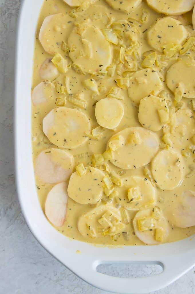Sliced potatoes and onions with broth in a baking dish.
