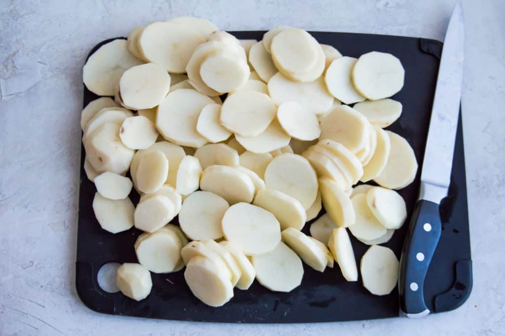Sliced potatoes on a cutting board with a knife. 