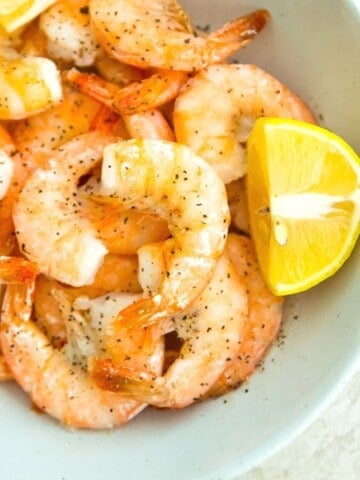 A bowl of cooked shrimp with lemon wedges beside them.