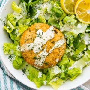 A salmon cake on a bed of lettuce drizzled with aioli sauce.