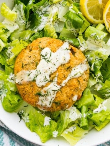 A salmon cake on a bed of lettuce drizzled with aioli sauce.