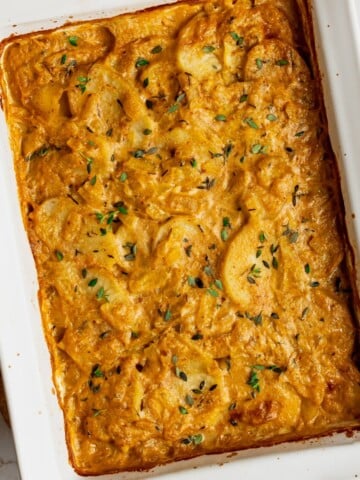 A pan filled with cooked dairy free scalloped potatoes garnished with fresh thyme.