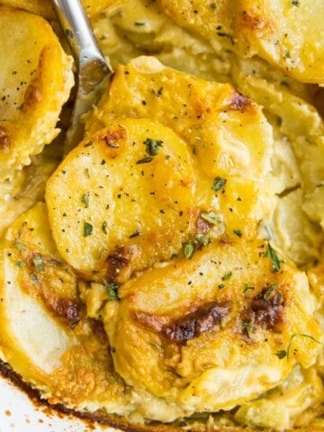 A pan filled with dairy free scalloped potatoes with a serving spoon in it.