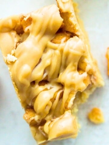 A paleo apple pie bar with a bite out of it and pieces of cooked apples beside it.