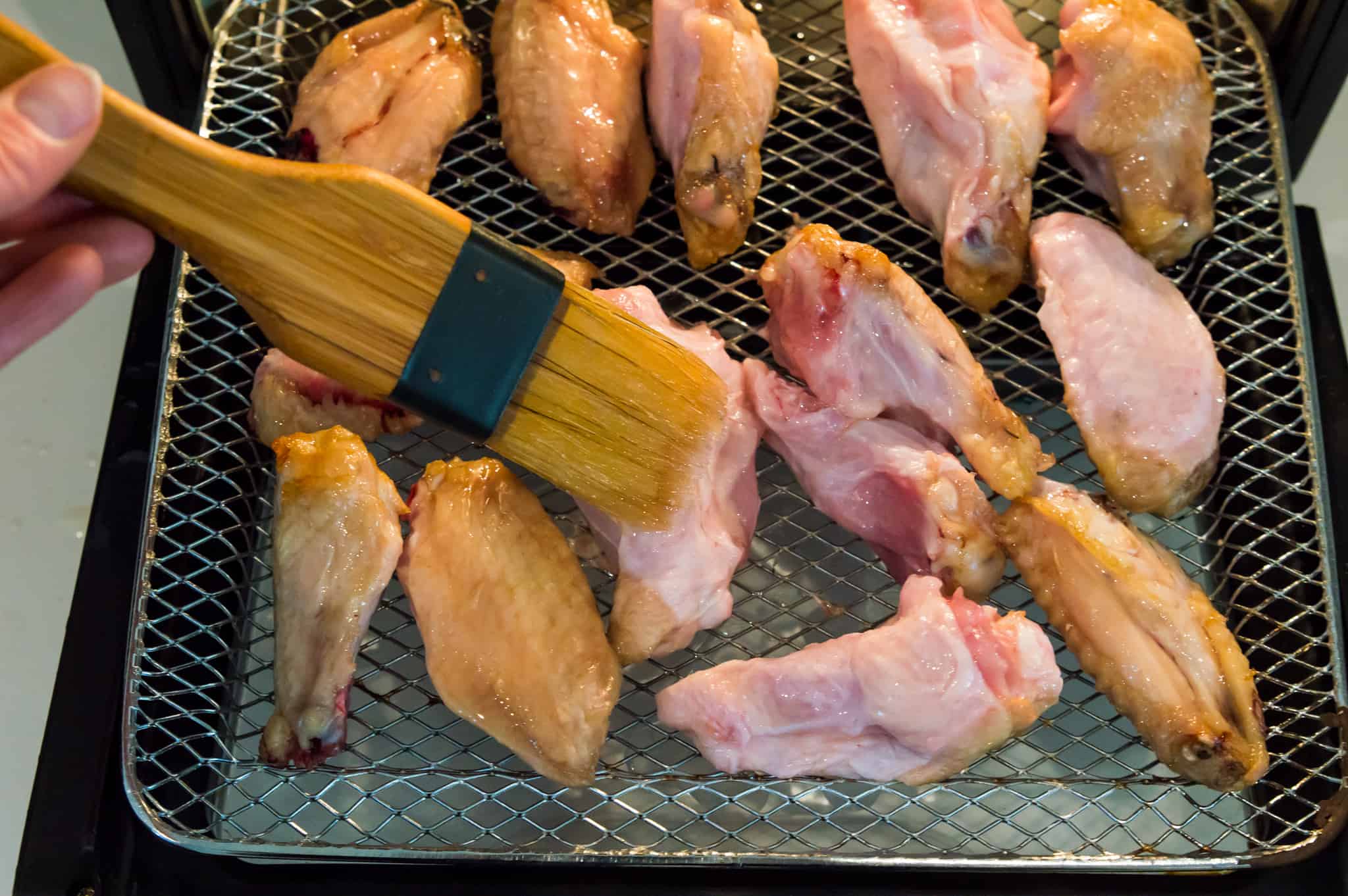 Chicken wings on an air fryer tray being brushed with oil. 