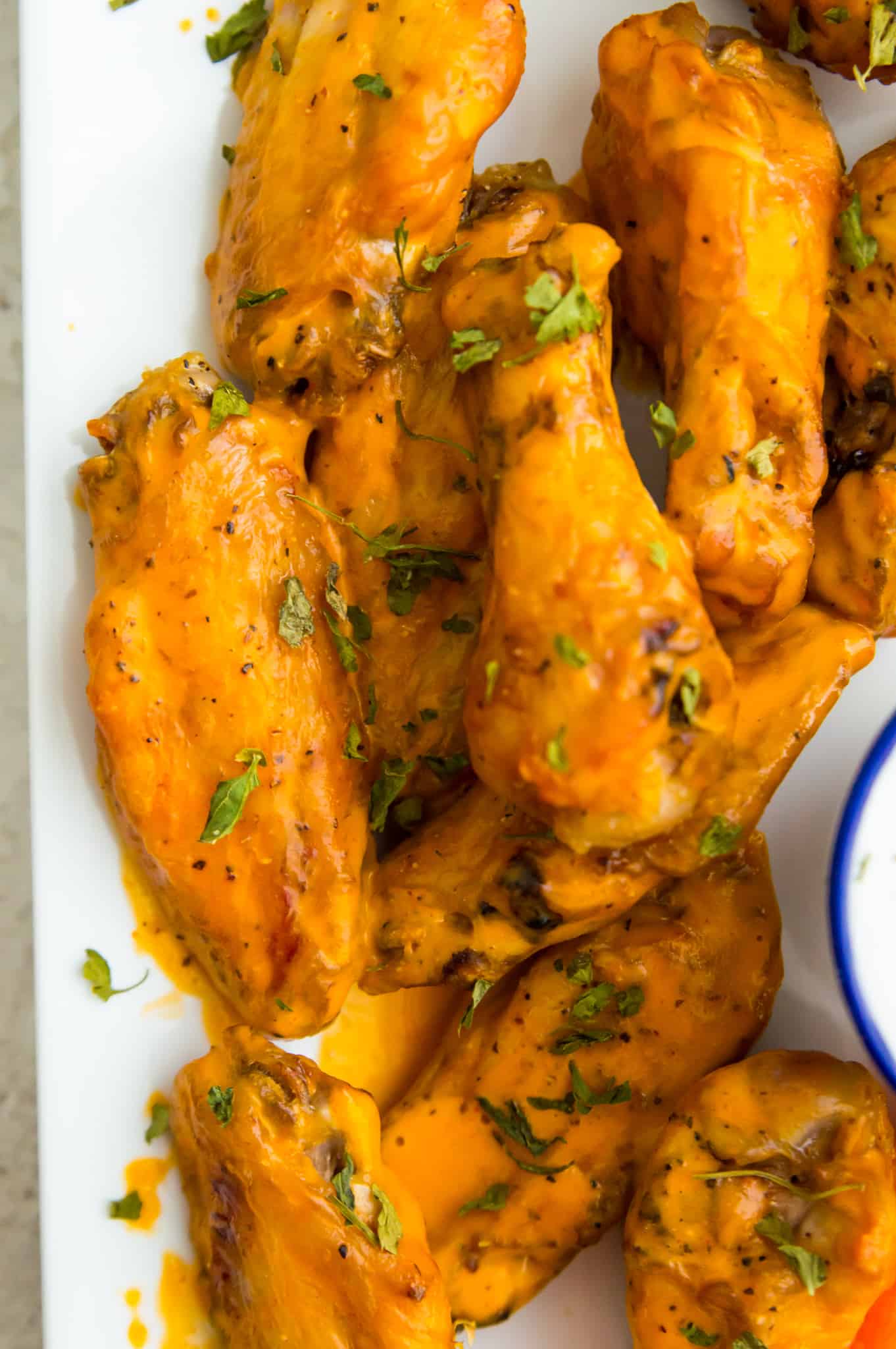 A plate full of cooked chicken wings coated in buffalo sauce.