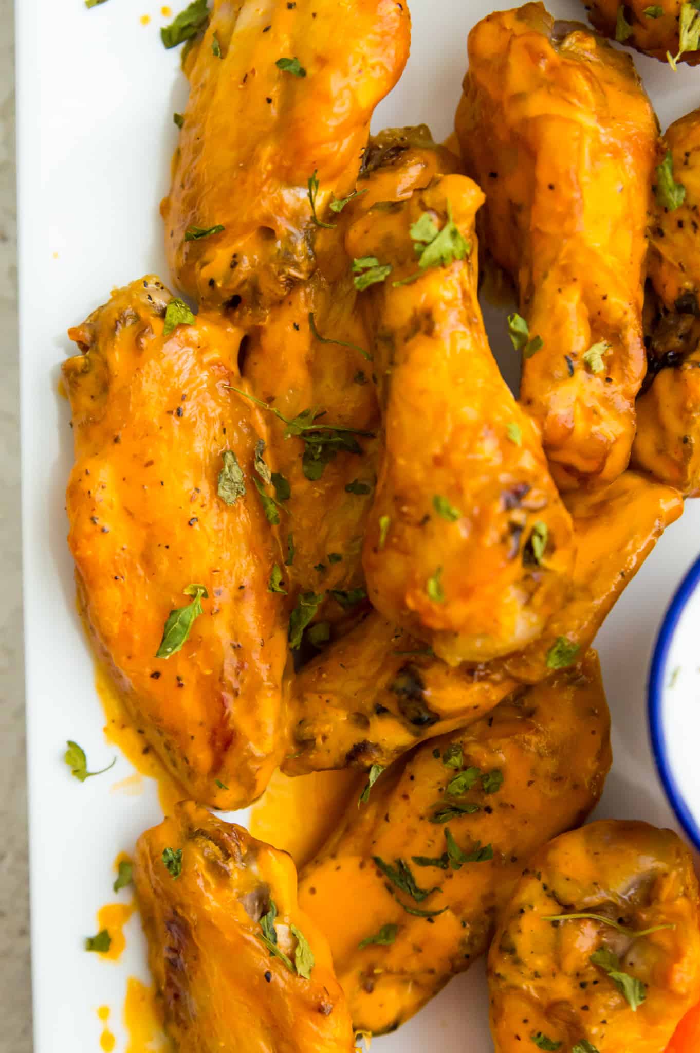 A plate full of cooked chicken wings coated in buffalo sauce. 