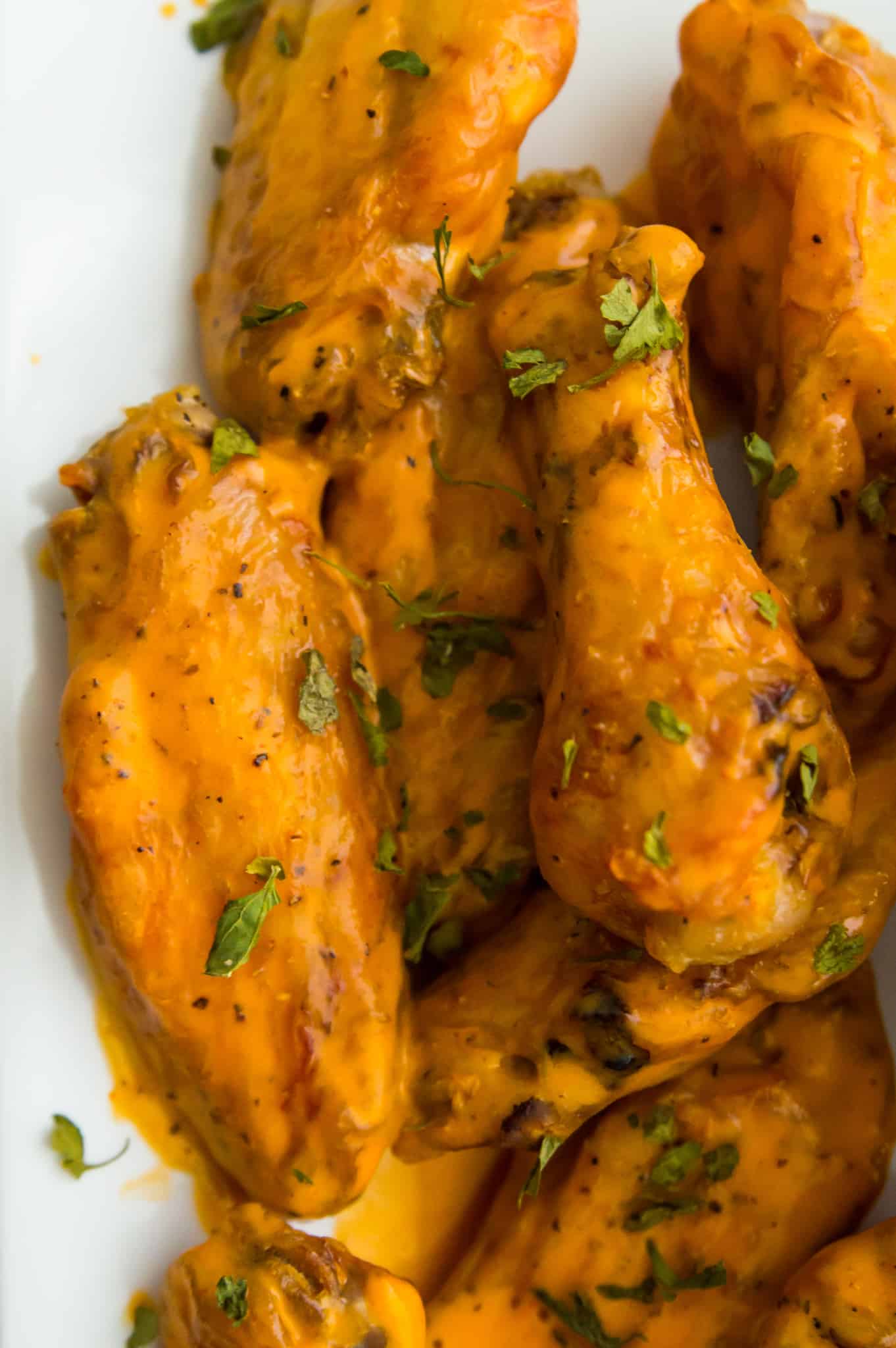 A plate full of cooked chicken wings covered in buffalo sauce and garnished with parsley.