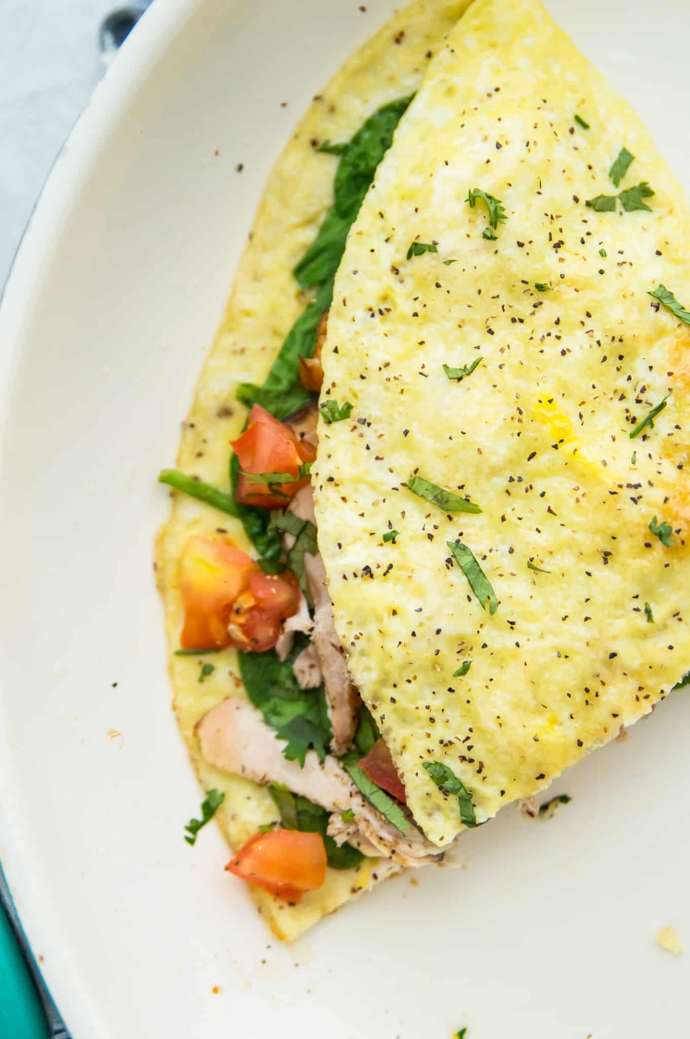 A chicken omelette that has been cut in half and filled with tomato and spinach.