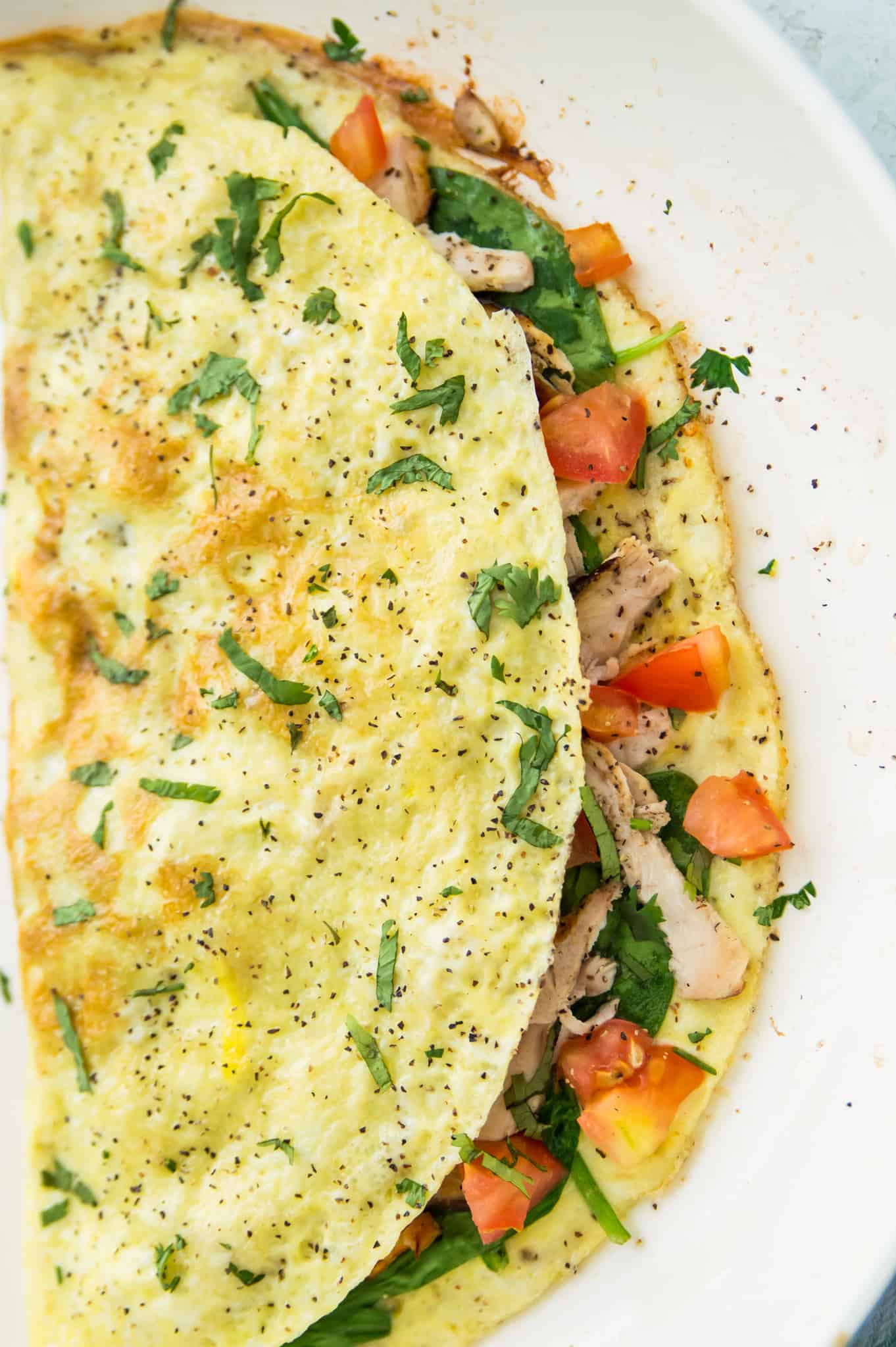 A chicken omelette filled with tomato and spinach and garnished with cilantro on a plate.