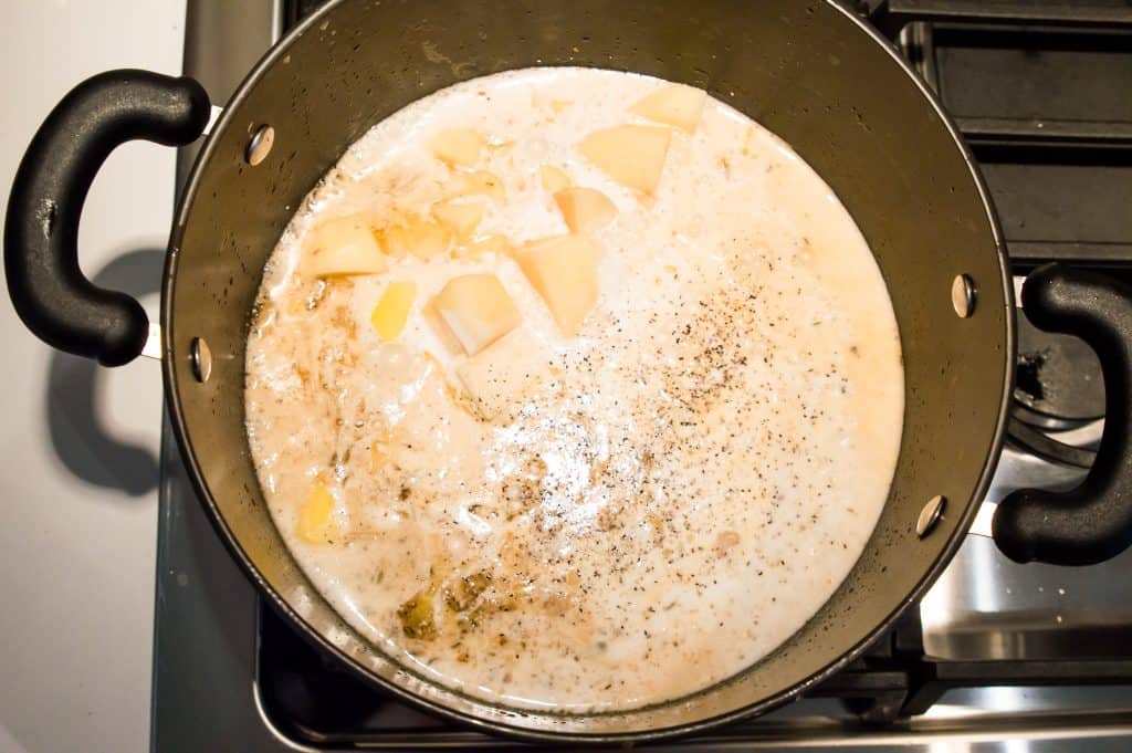 A pot on the stovetop with coconut milk, spices and chopped potatoes cooking in it.