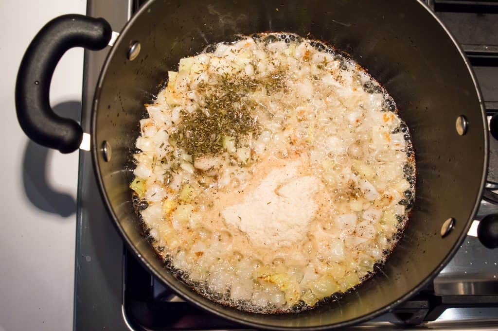 A pot on the stove with chopped onions and spices cooking in it.