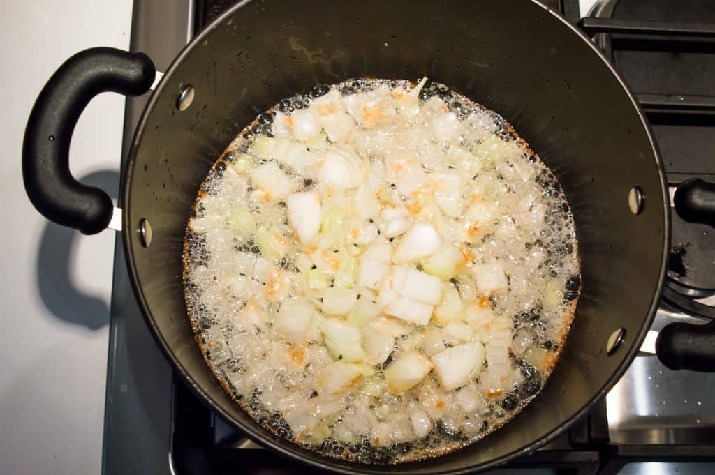 A pot on the stovetop with chopped white onions being cooked in it.