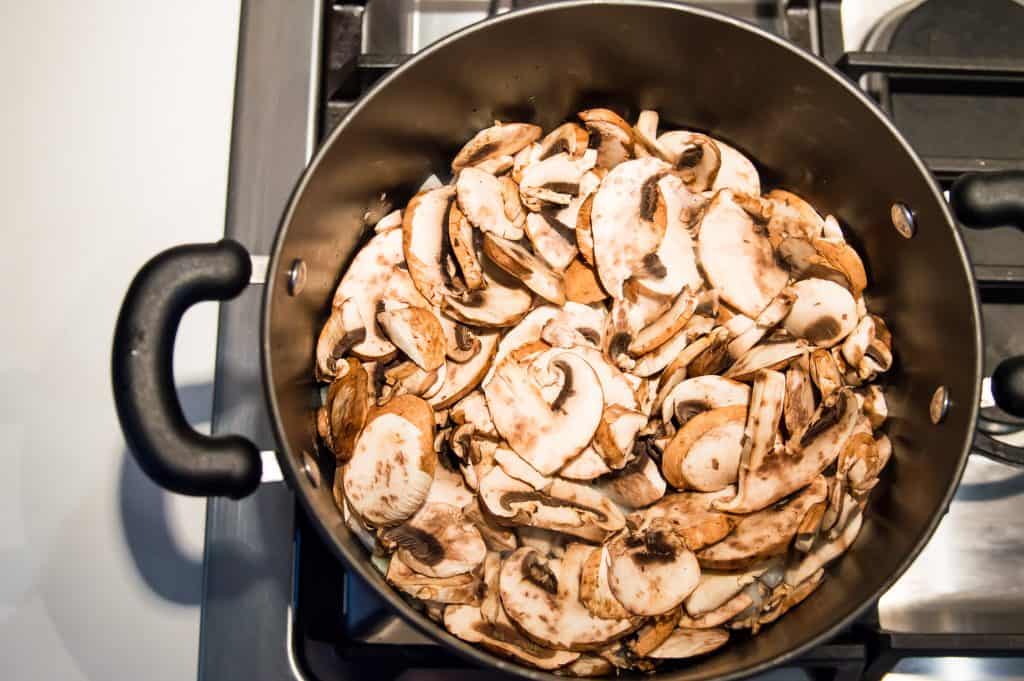 A large pot on the stove with fresh, chopped mushrooms in it.