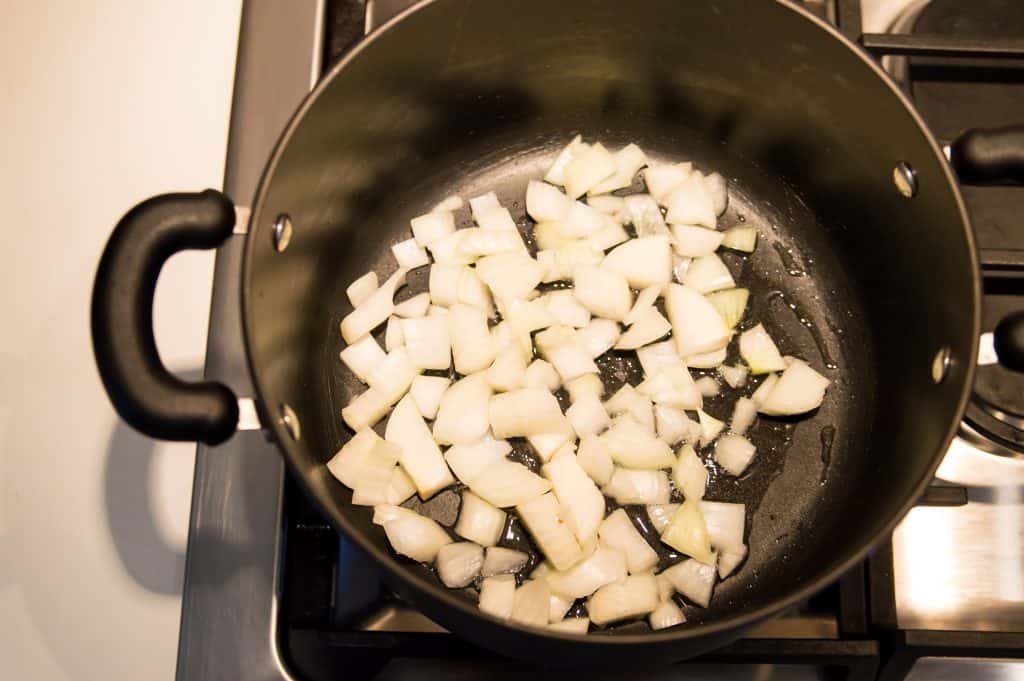 A large pot on the stove with chopped onions cooking in it.