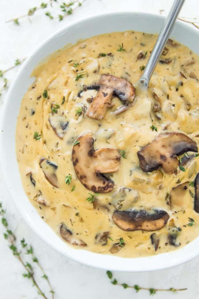 A bowl of vegan cream of mushroom soup topped with mushrooms with a spoon in the bowl