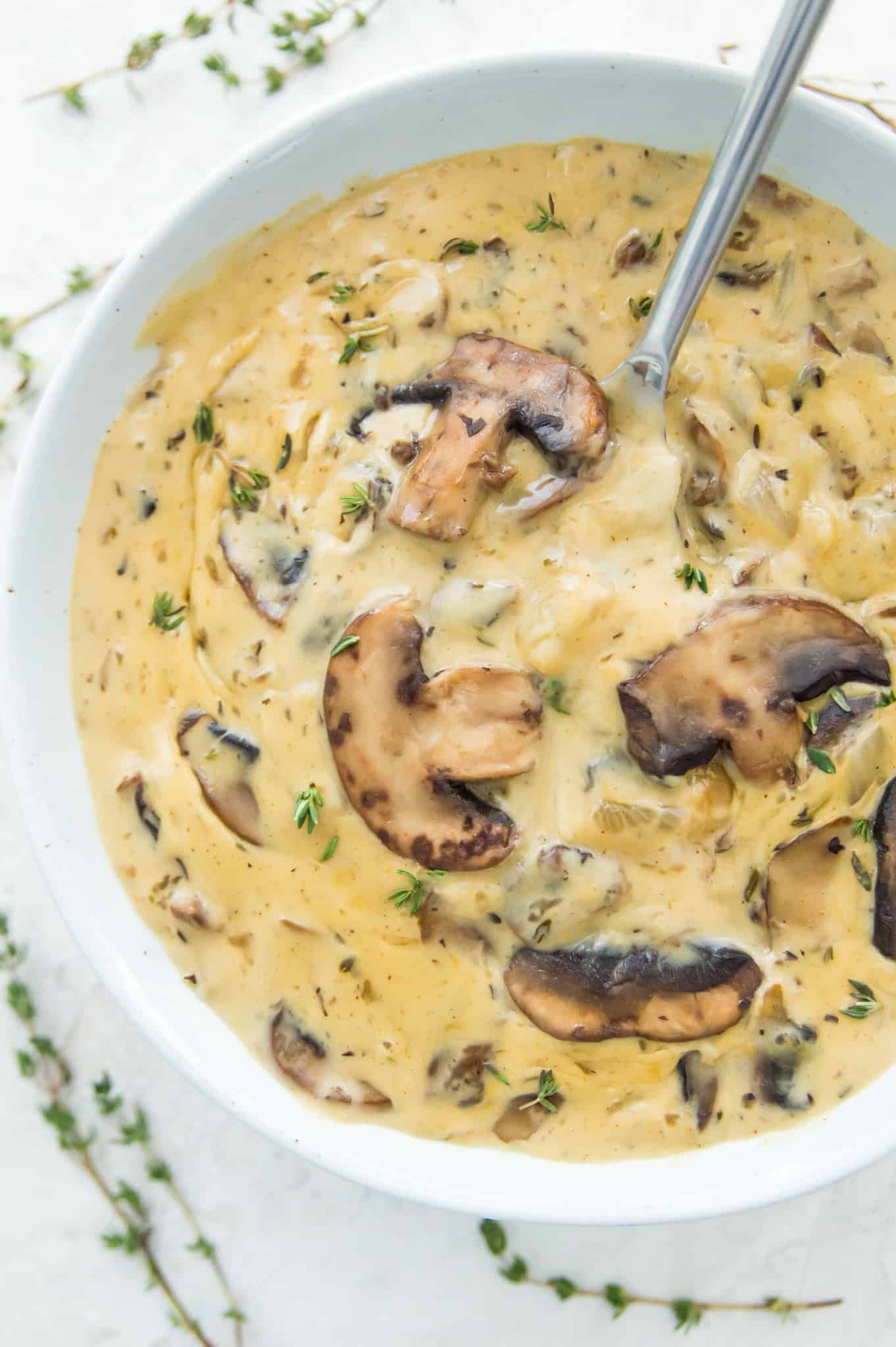 A bowl of vegan cream of mushroom soup topped with cooked mushrooms and with a spoon in the bowl.