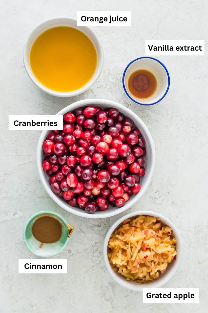 The ingredients for cranberry sauce in bowls including cranberries, orange juice, grated apple, cinnamon and vanilla extract.