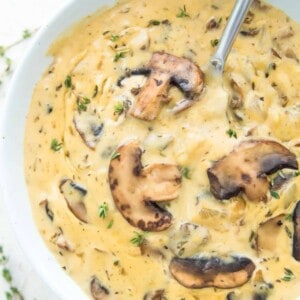 A bowl of vegan cream of mushroom soup with a spoon in it and topped with cooked mushrooms.