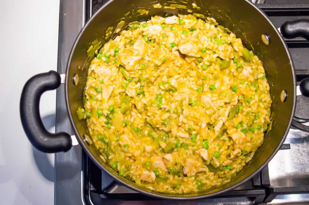 A large pot on the stove with chicken leek risotto with peas cooking in it.