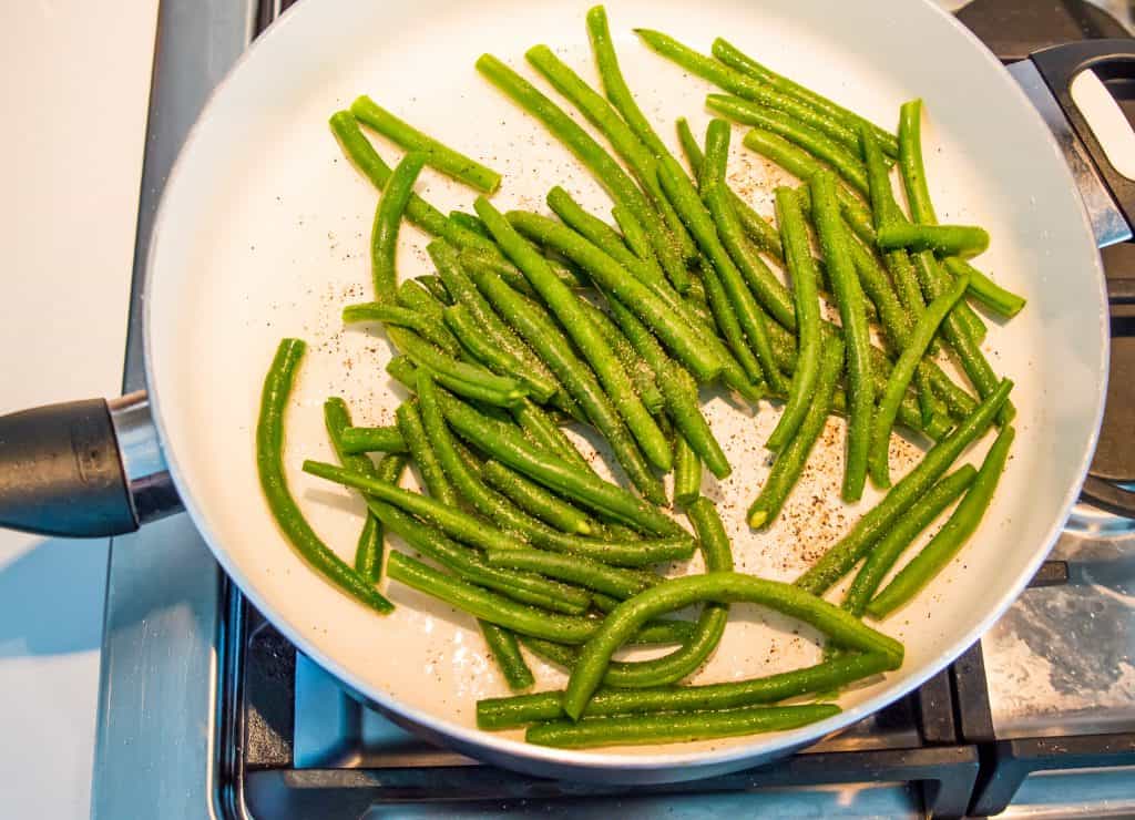 Fresh green beans cooking in a pan on the stovetop.