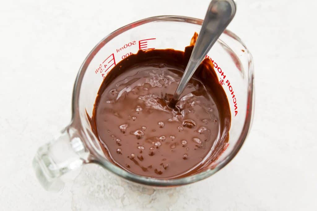 Melted chocolate in a glass measuring cup with a spoon in it.