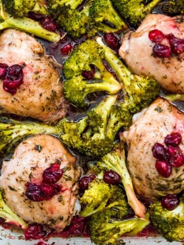 A pan filled with cooked chicken thighs surrounded by cooked broccoli and topped with cranberries.