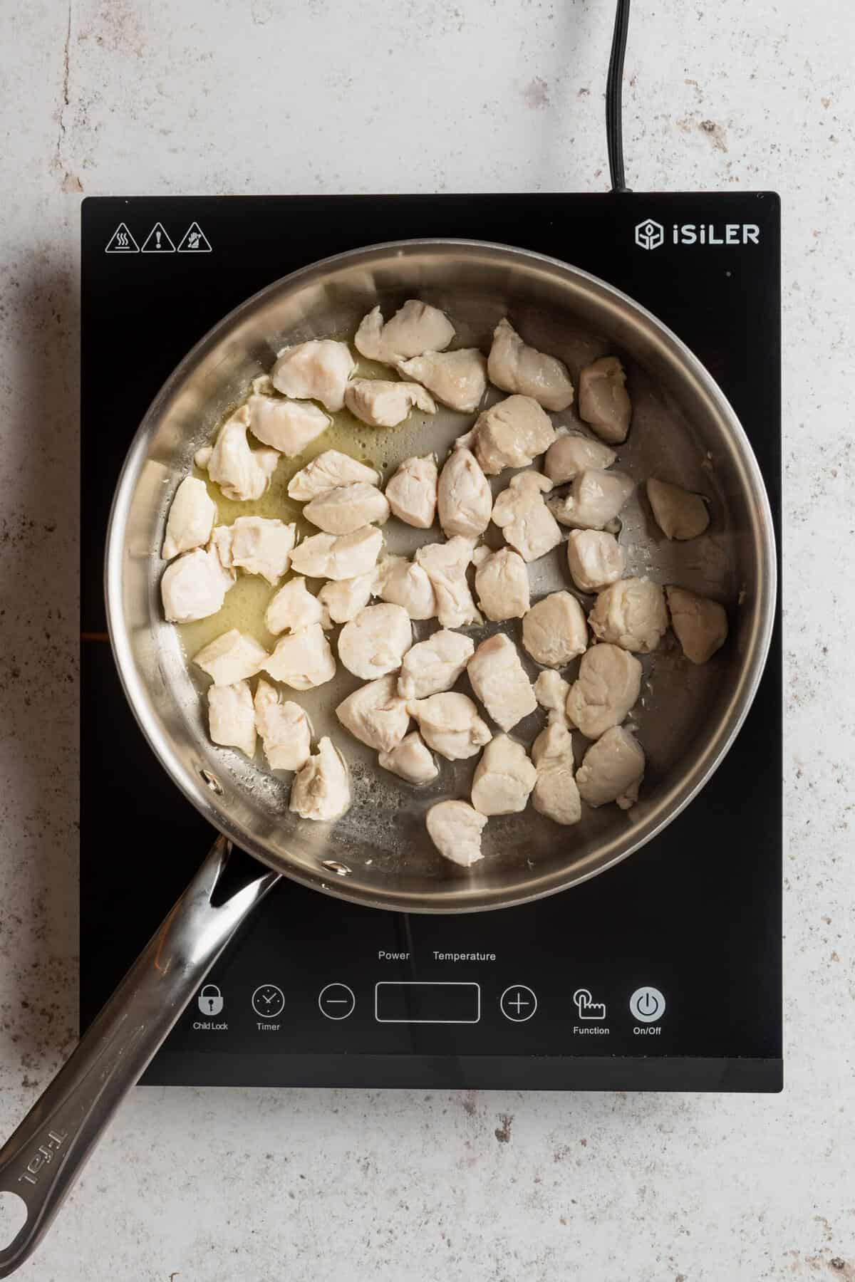 A pot with chicken pieces being cooked in it.
