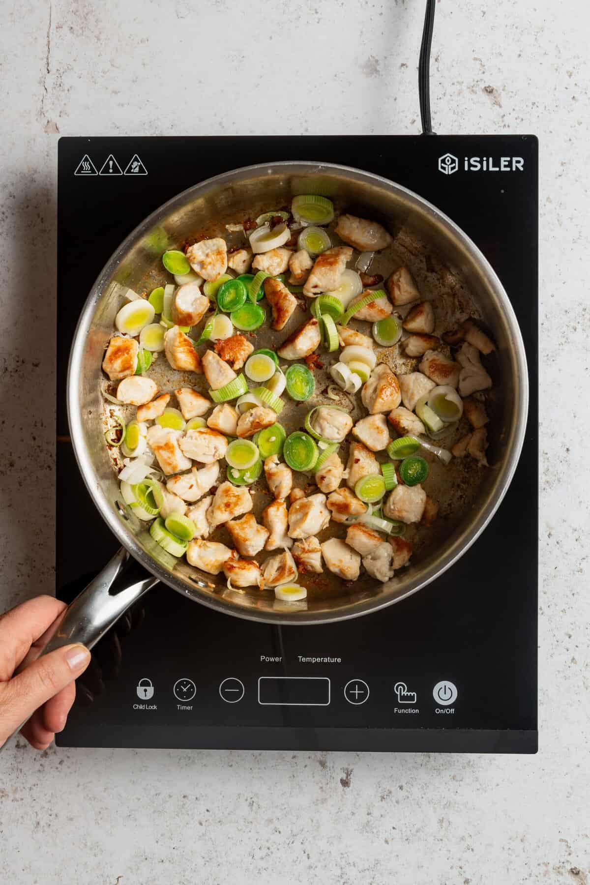 A pot with chicken pieces and chopped leaks being cooked in it.