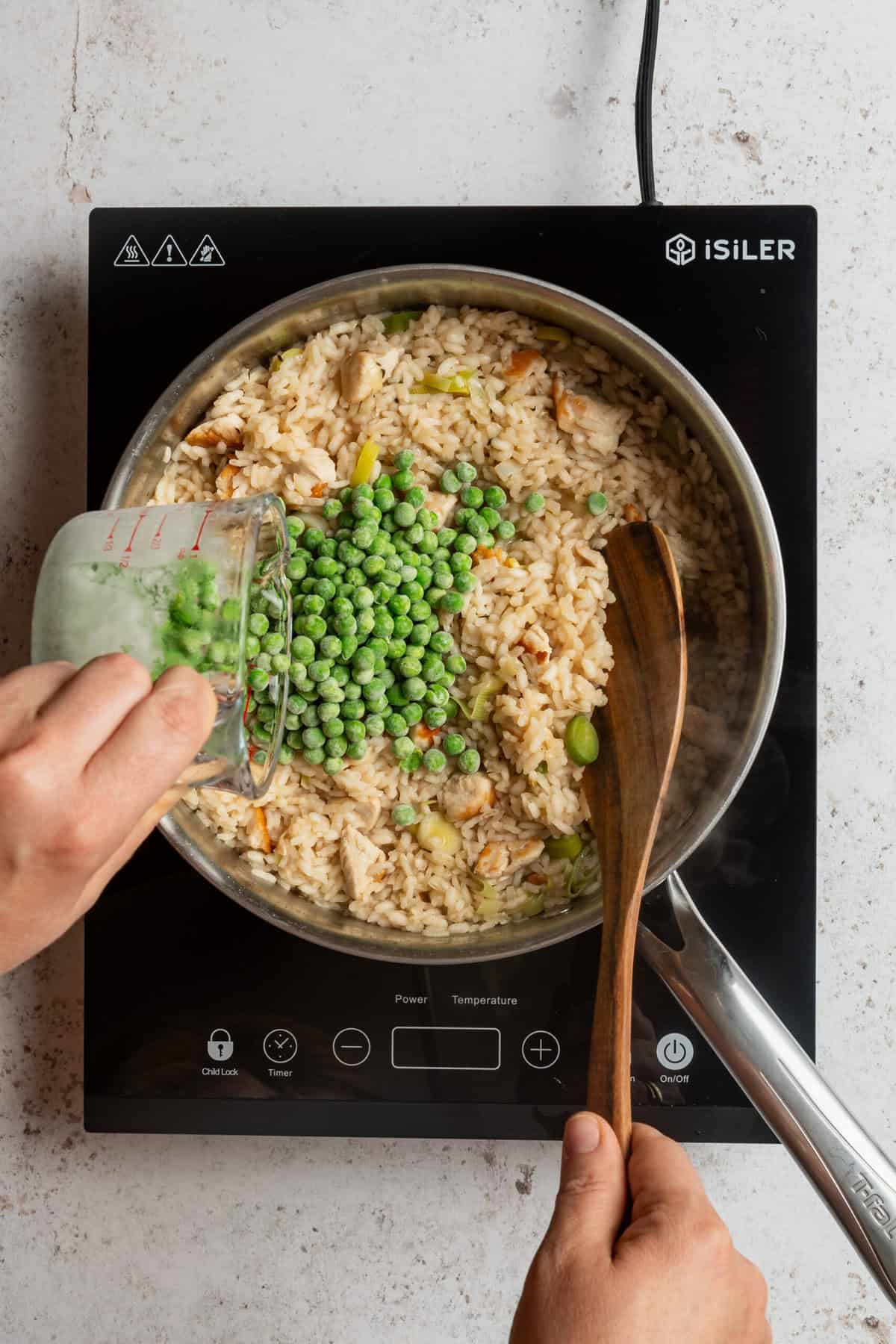 A pot filled with cooked rice with frozen green peas being poured into it.