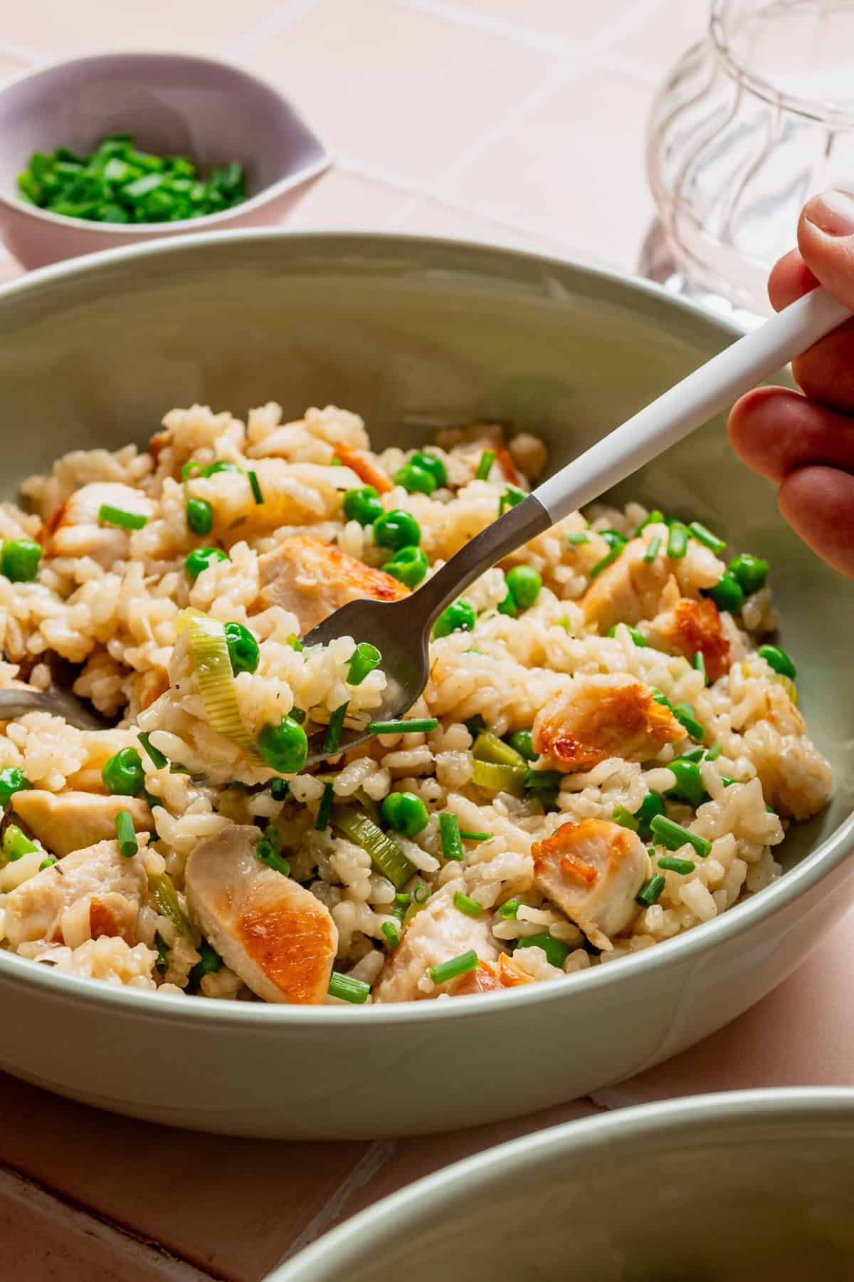 A bowl filled with chicken and leek risotto with green peas with a fork taking some of the risotto out of the bowl.