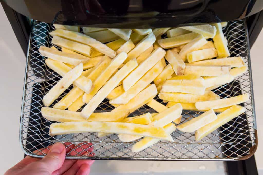 Frozen French fries on an air fryer tray. 