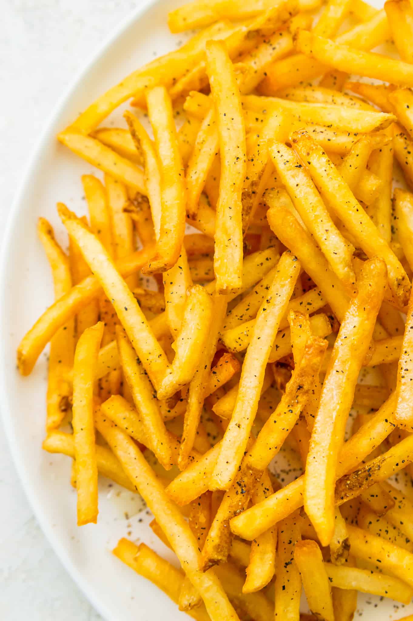 A plate of cooked French fries seasoned with salt and pepper. 