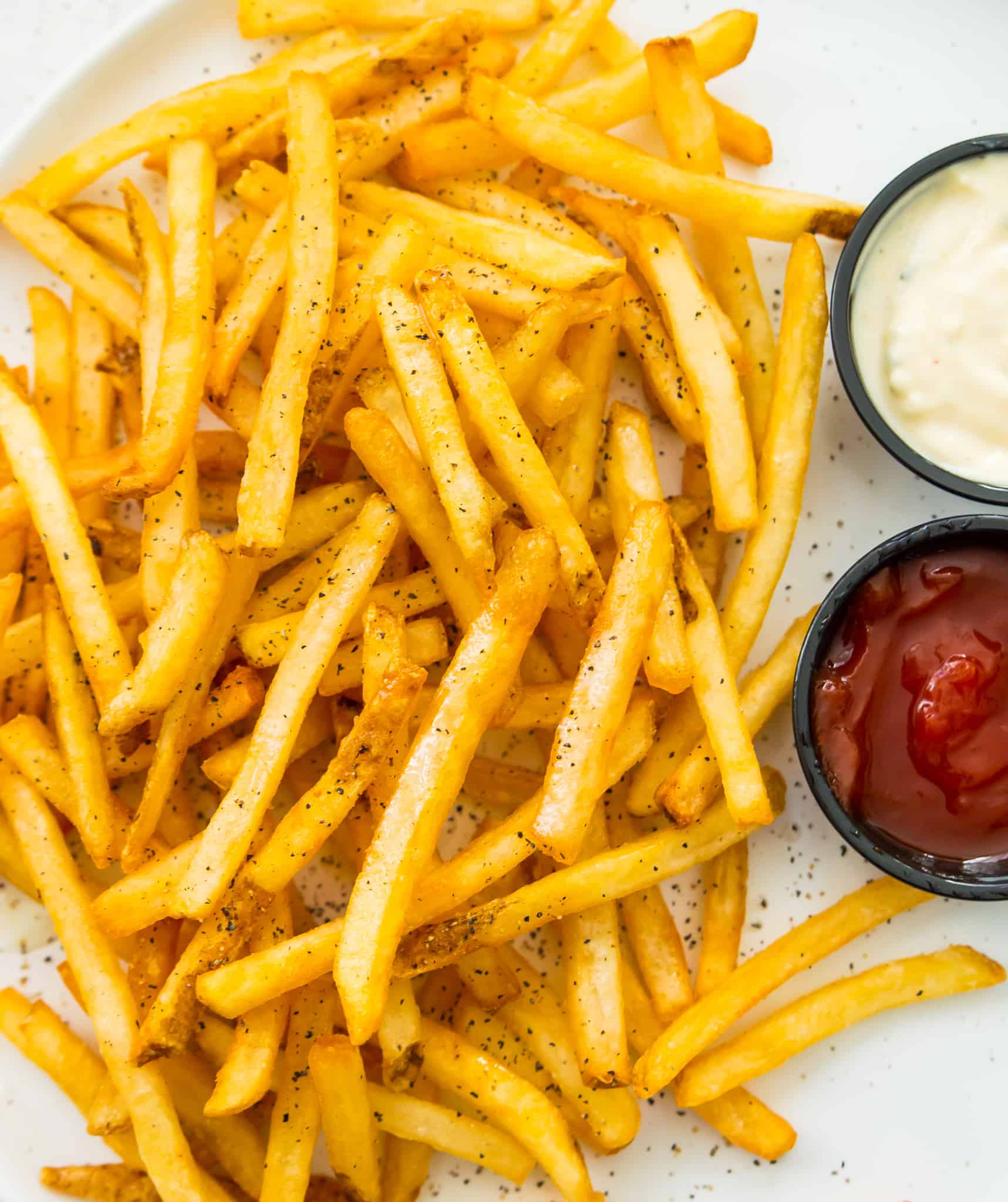 A plate of cooked French fries with ketchup and mayonnaise beside it.