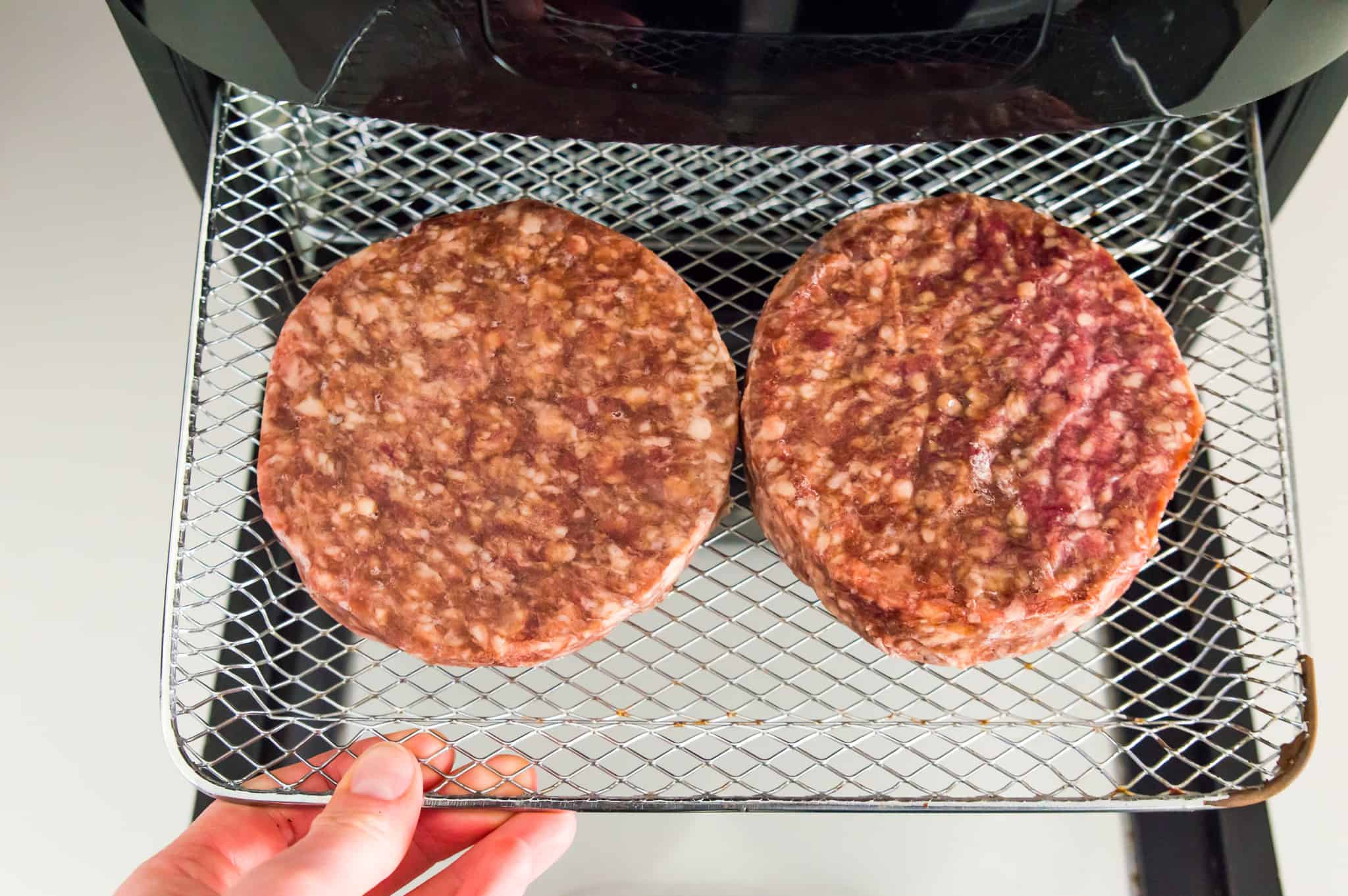 Frozen hamburger patties on an air fryer tray. 