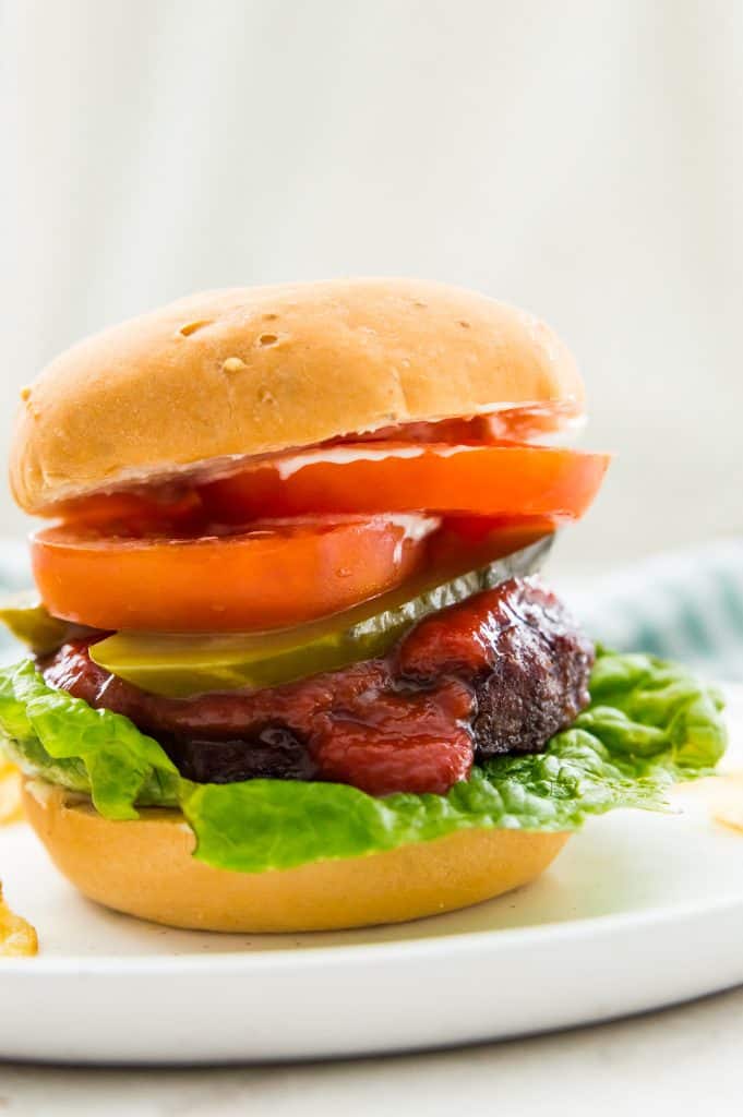 An air fryer frozen hamburger in a bun with sliced tomatoes and pickles 