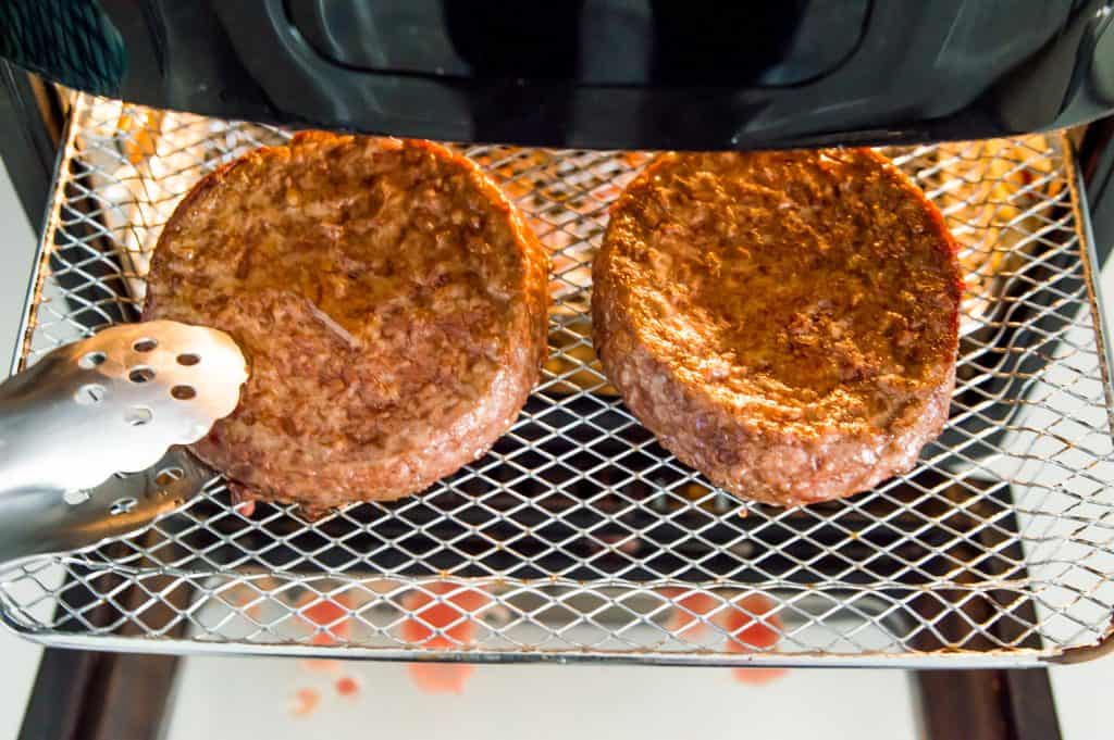 Two hamburger patties cooking on an air fryer tray. 