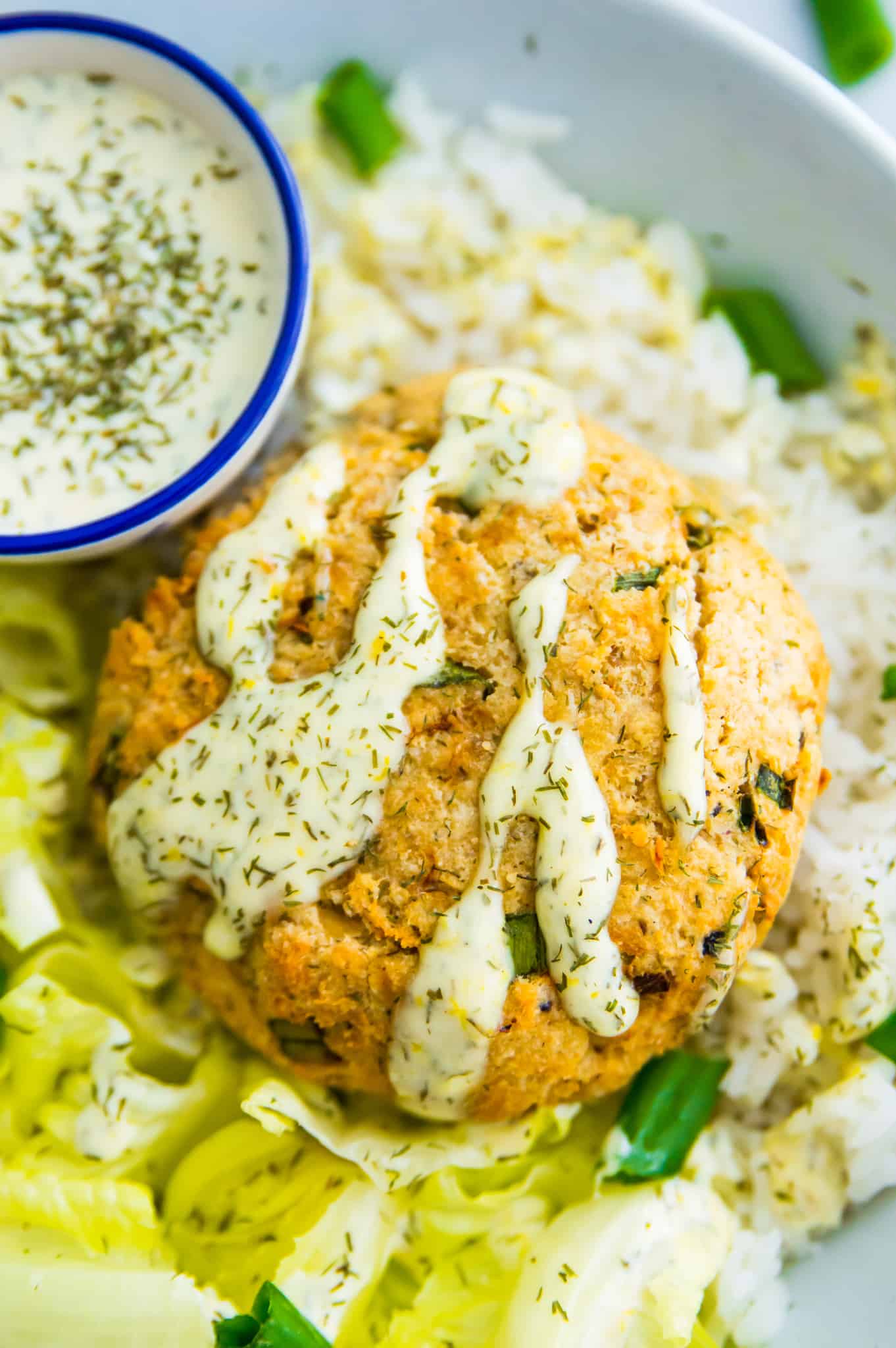 A cooked salmon cake on a bed of chopped lettuce, topped with a creamy aioli sauce. 