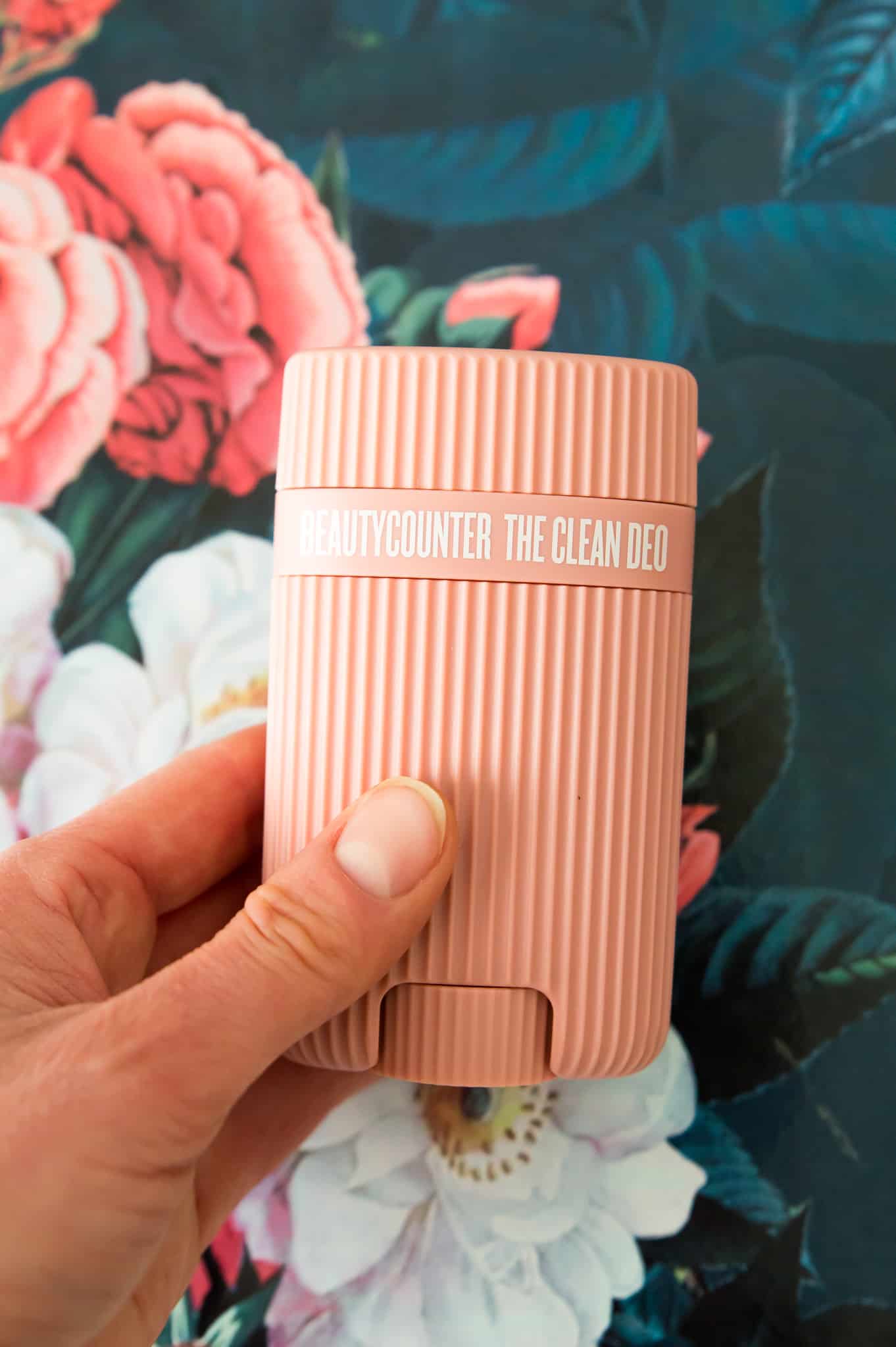 A hand holding the Beautycounter deodorant over a floral background. 