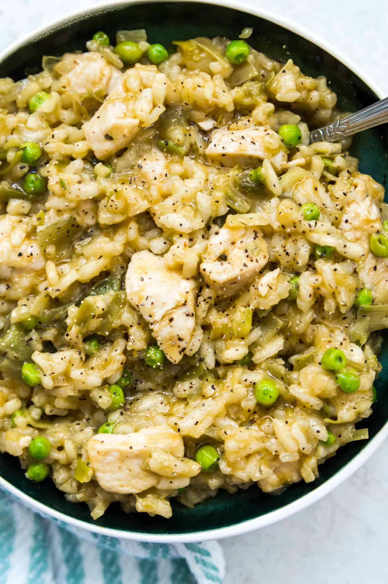 A bowl of chicken and leek risotto with peas and a spoon in it.