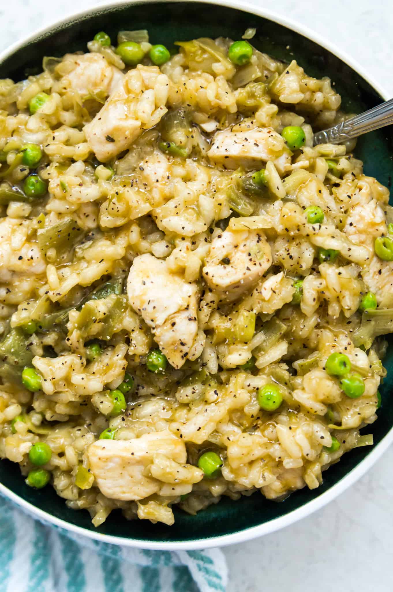 A bowl of creamy chicken leek risotto with peas and a spoon in it.