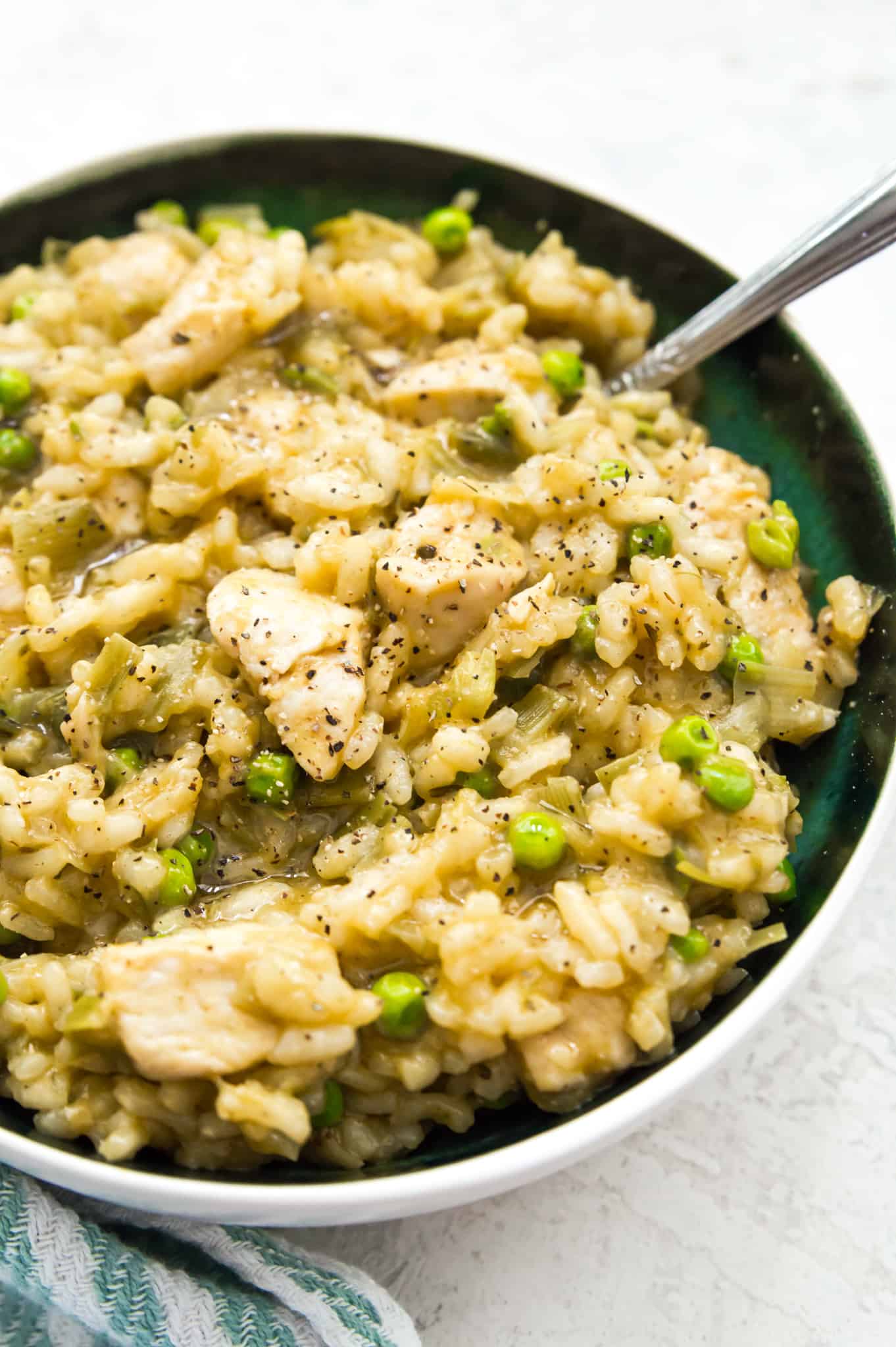 A bowl of chicken and leek risotto with peas on top and a spoon in it.
