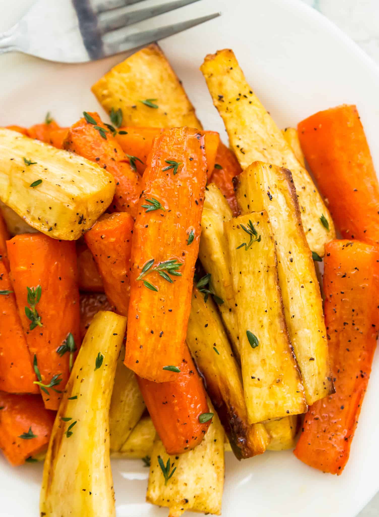 A plate full of honey glazed carrots and parsnips topped with fresh thyme.