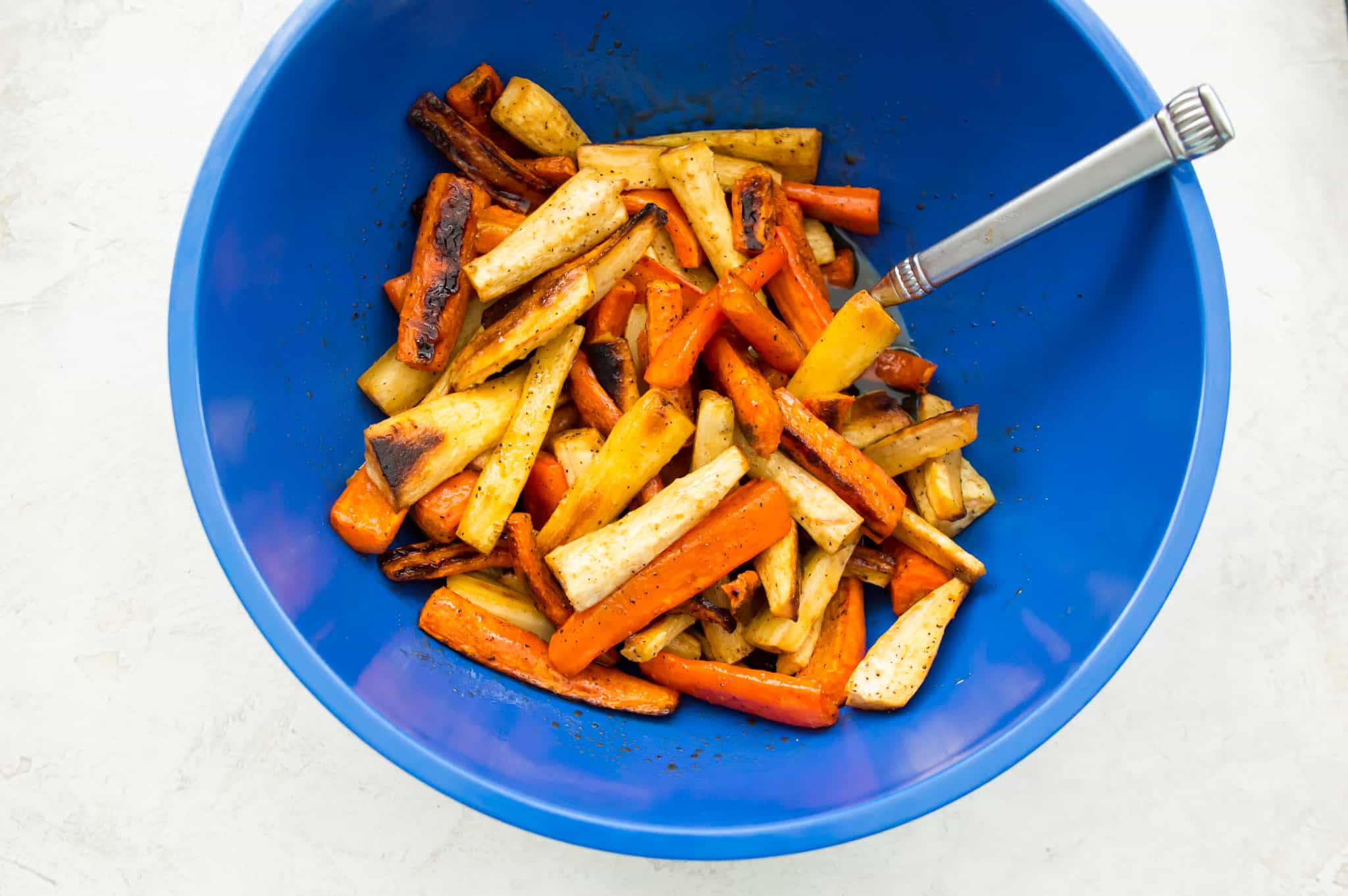 A bowl of roasted chopped carrots and parsnips with a glaze on them.