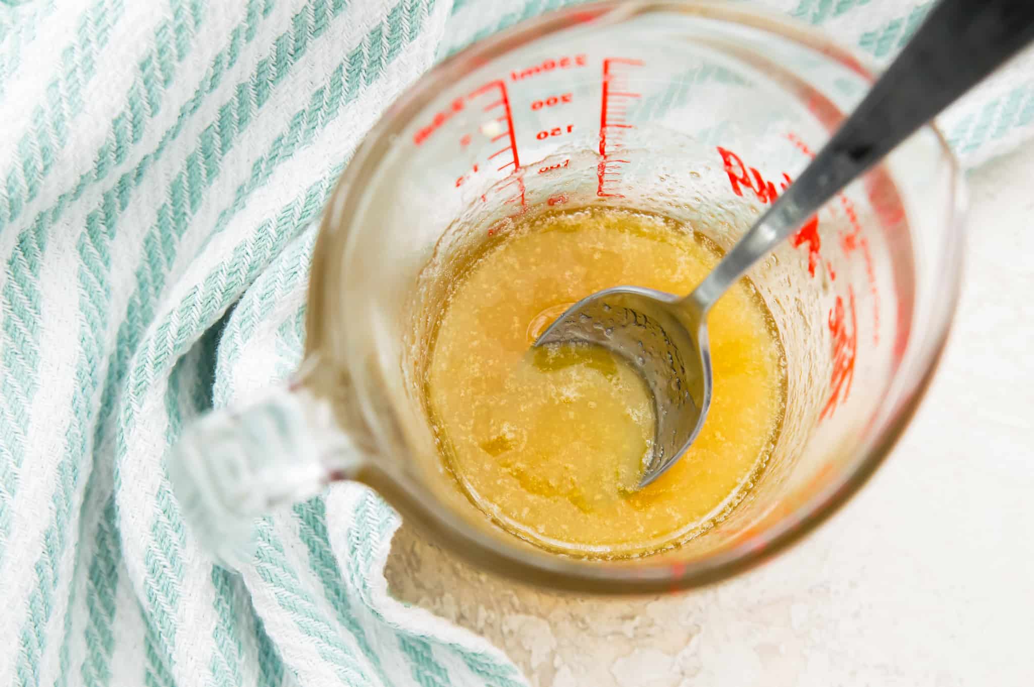 A glass measuring cup filled with a honey glaze with a spoon in it.