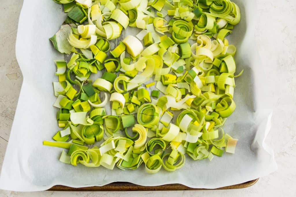 A baking sheet with parchment paper on it covered in chopped leeks. 