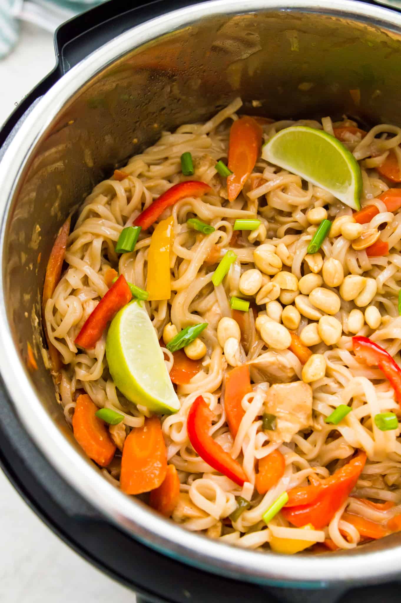 A large batch of Instant Pot Pad Thai with lime wedges and peanuts inside an Instant Pot.