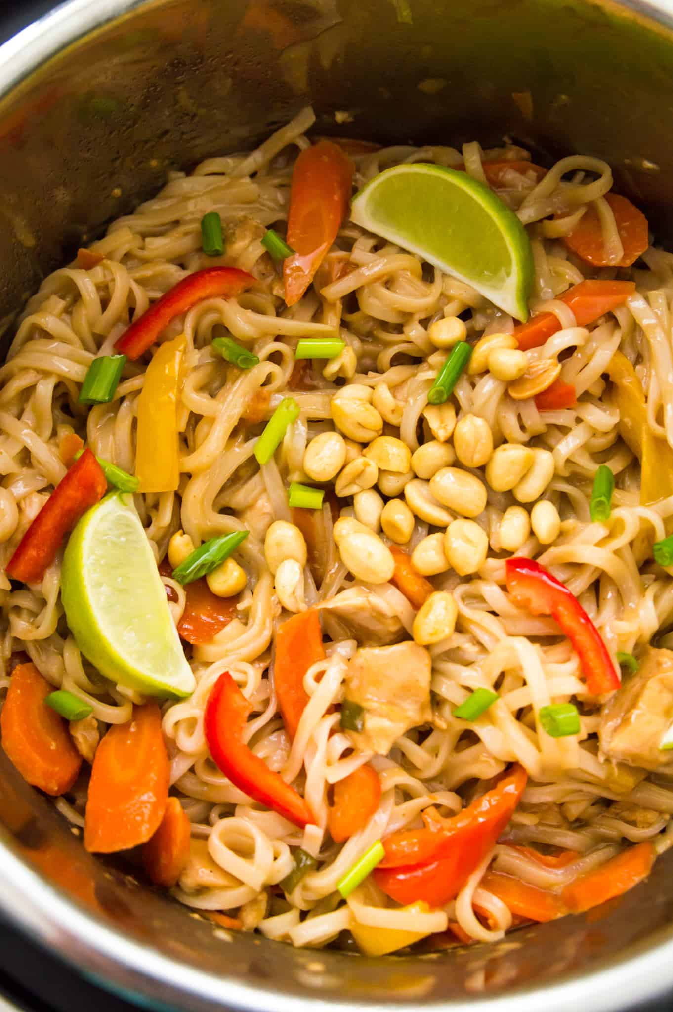 An Instant Pot with chicken pad Thai in it topped with lime wedges and peanuts.