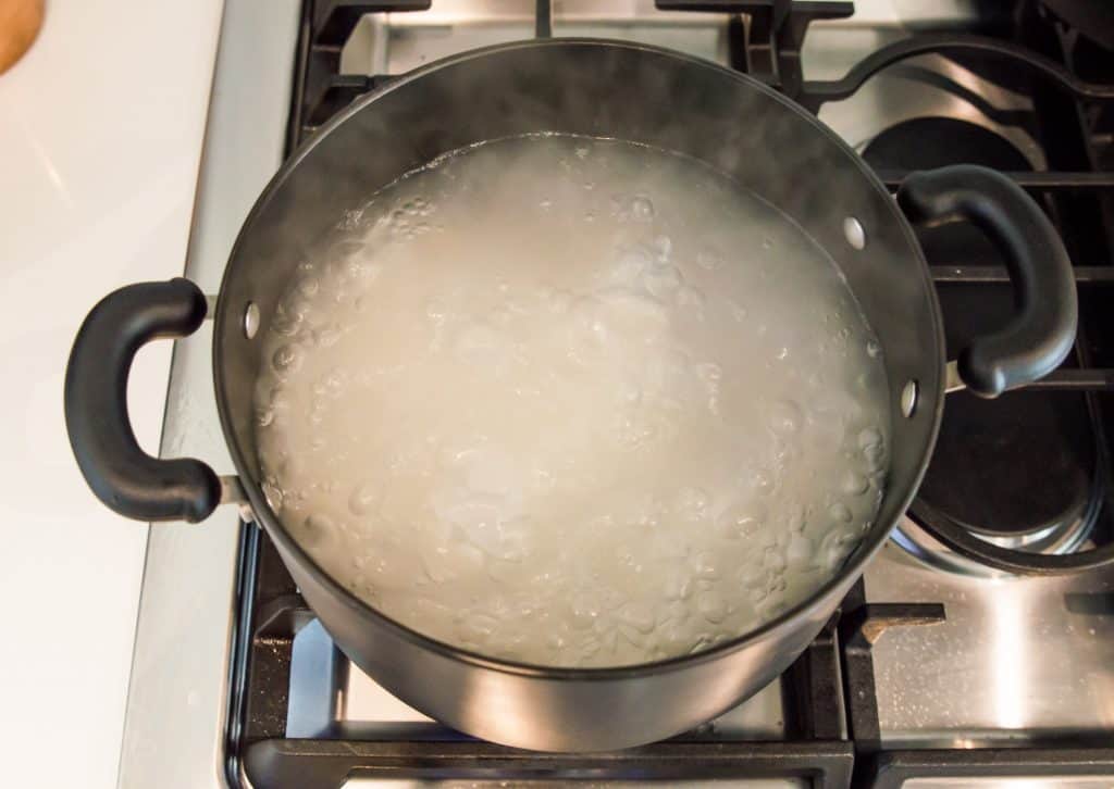 A pot of boiling water on a stovetop with rice noodles cooking in it. 
