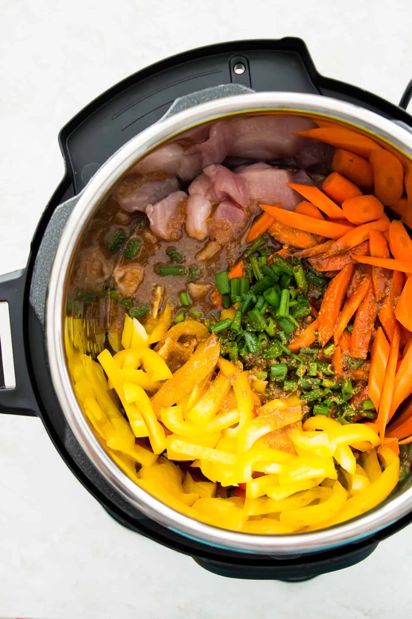 An Instant Pot with chopped peppers, chicken, carrots and green onion in it.